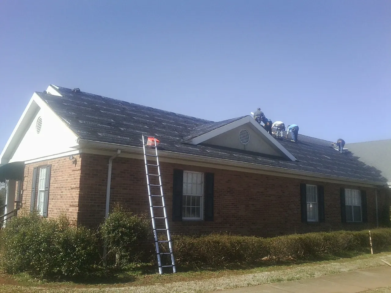 Crew tearing shingles off a brick ranch roof with a ladder set — Emergency Roof Repair work by our crew in Templeton