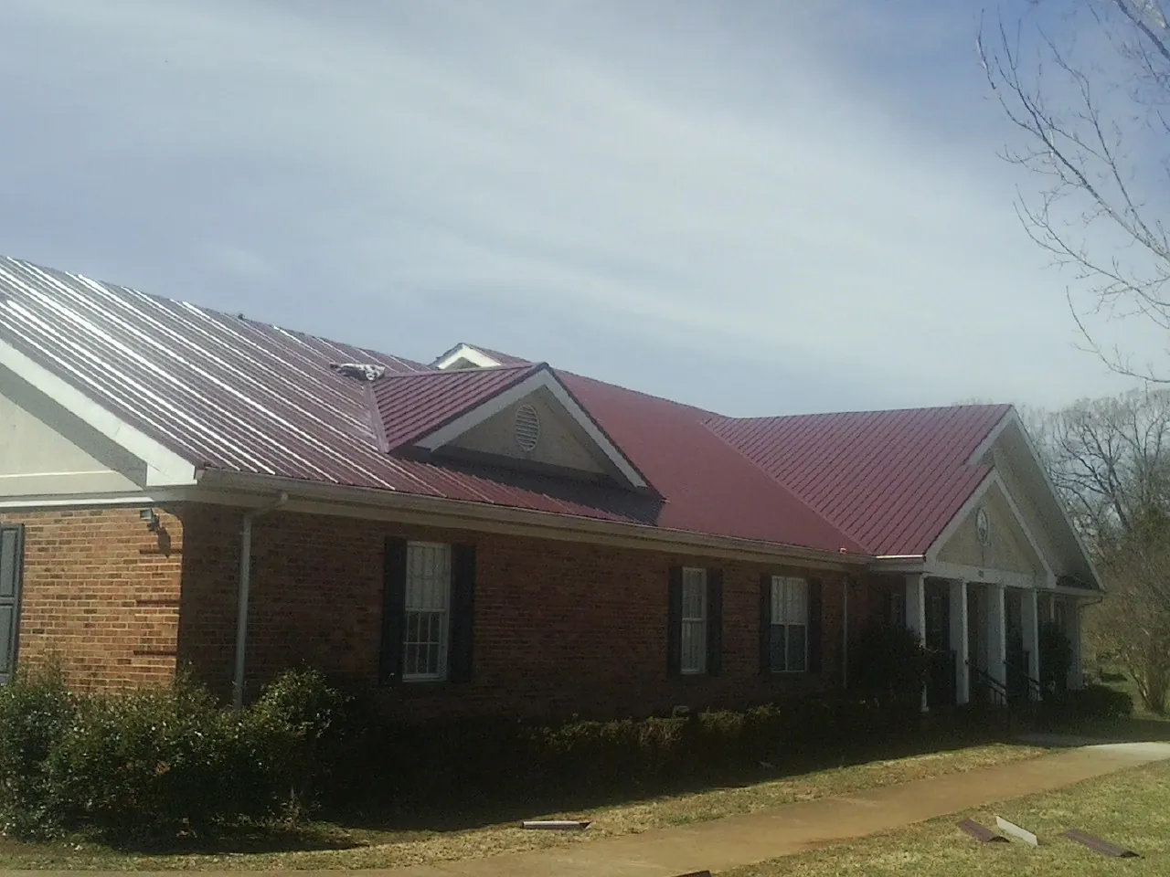 Red metal roof with gabled entries on a long brick building, from a Hail Damage Roof Repair job in Templeton